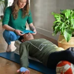 A teacher placing an eye pillow on a student lying back over a bolster
