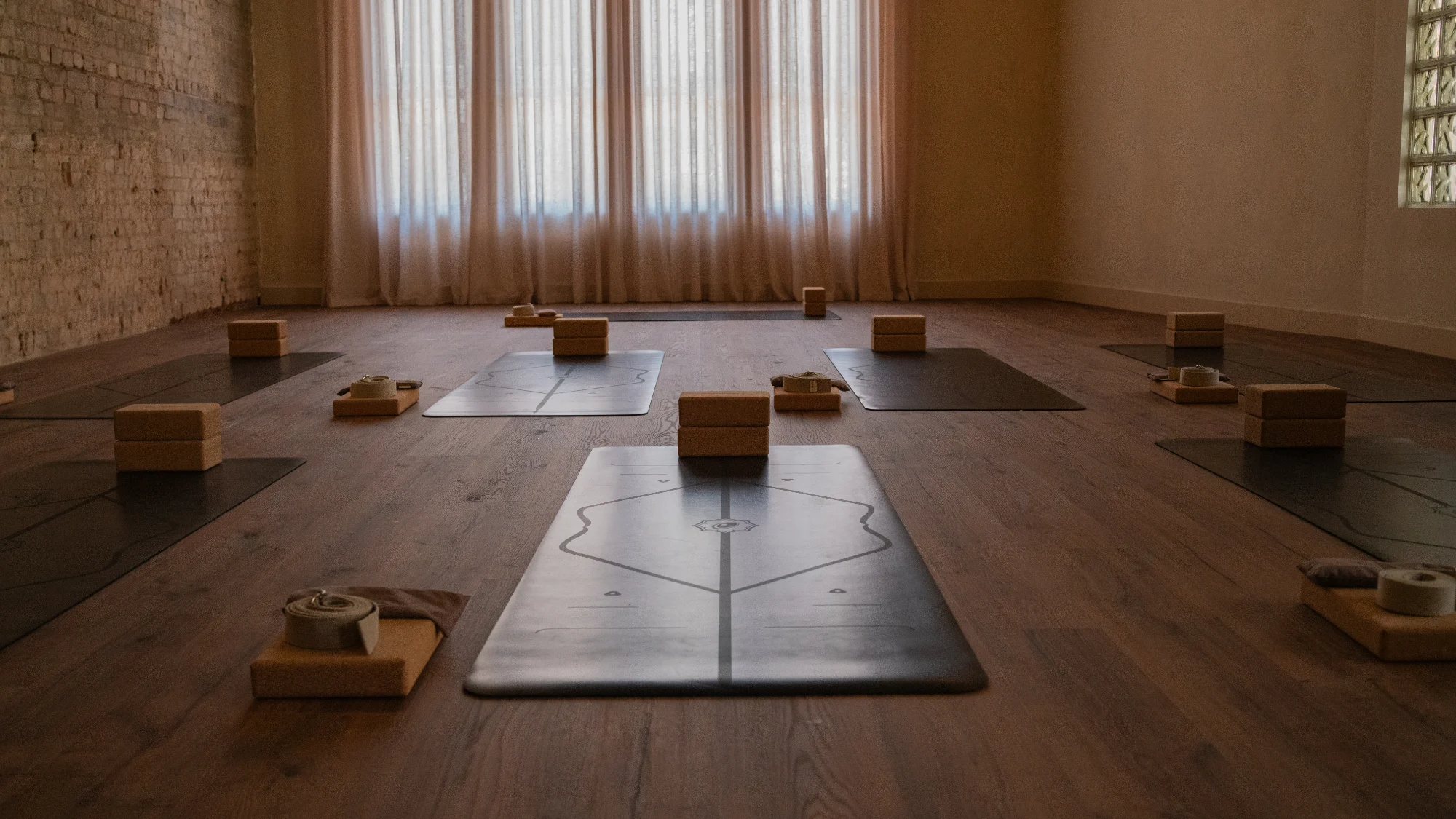 The yoga room with mats laid out, each with a cork block and bolster, in front of curtained windows
